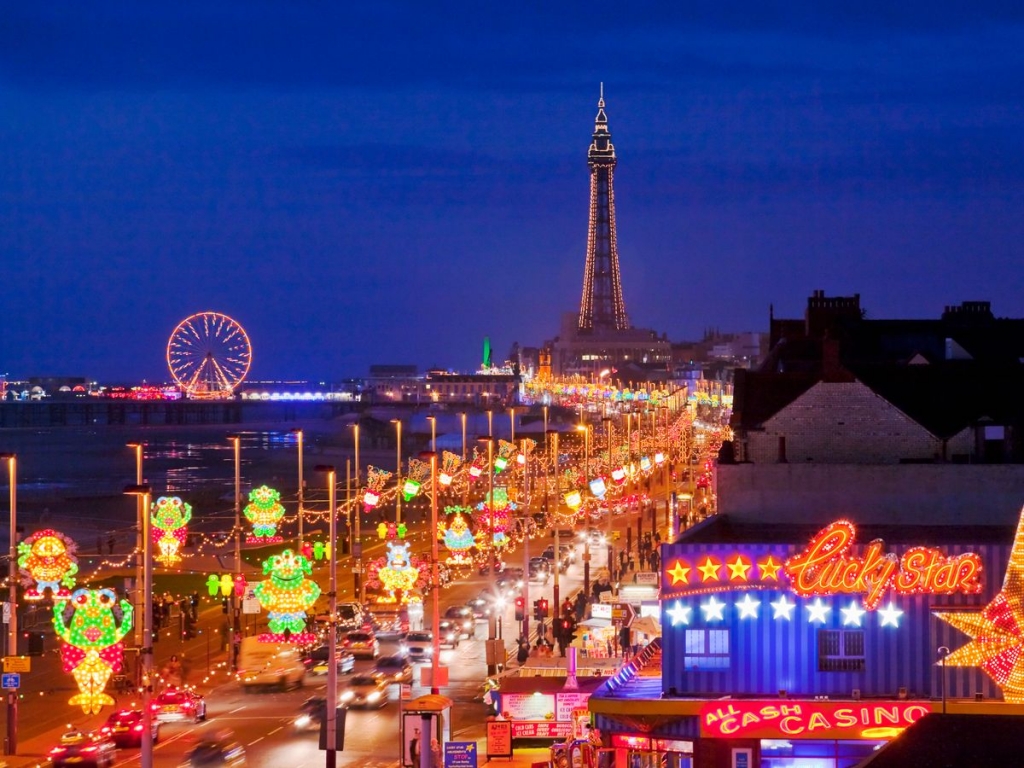 Blackpool Illuminations at night — the promenade lit up with colourful displays, Blackpool Tower and the Big Wheel in the background