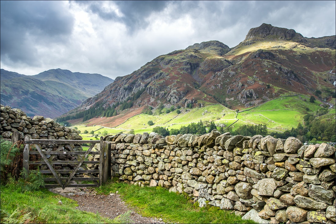 Dry stone wall and gate in Great Langdale, with the Langdale Pikes rising behind green valley fields