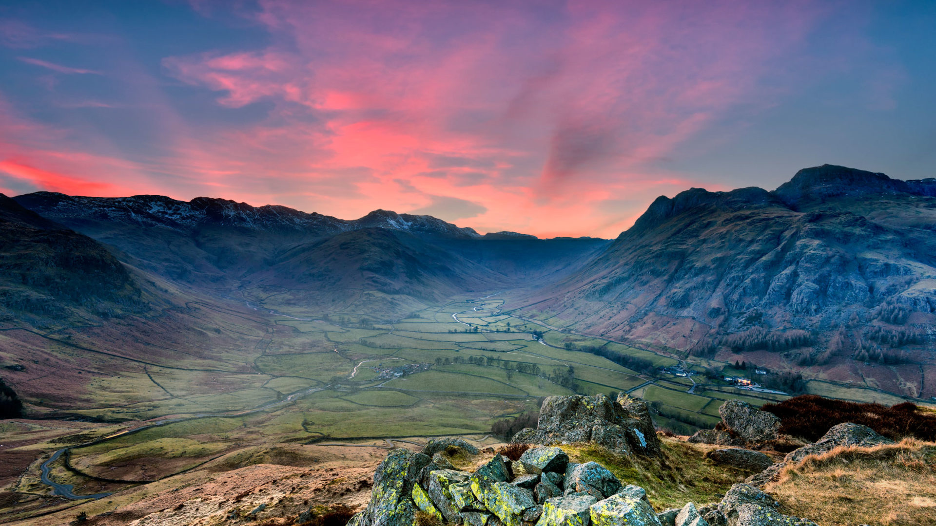 Sunset over the Langdale valley in the Lake District, viewed from the fells with pink sky and snow-capped mountains