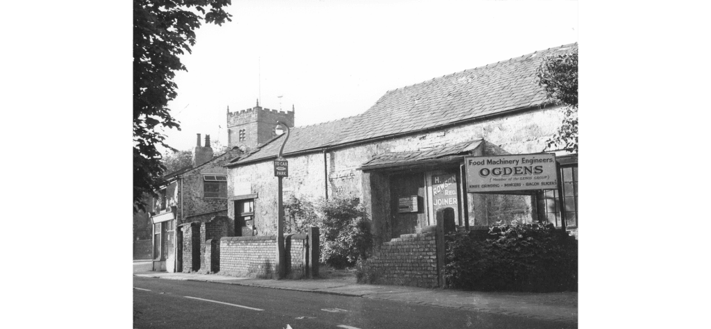 Tithebarn with signs for occupants - Ogdens Food Machinery Engineers and H Rowson, Joiner. Church behind.