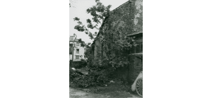 The Tithebarn in Poulton. We see the corner of an old building, a tree growing out of it, and an old wooden wheel in the foreground.